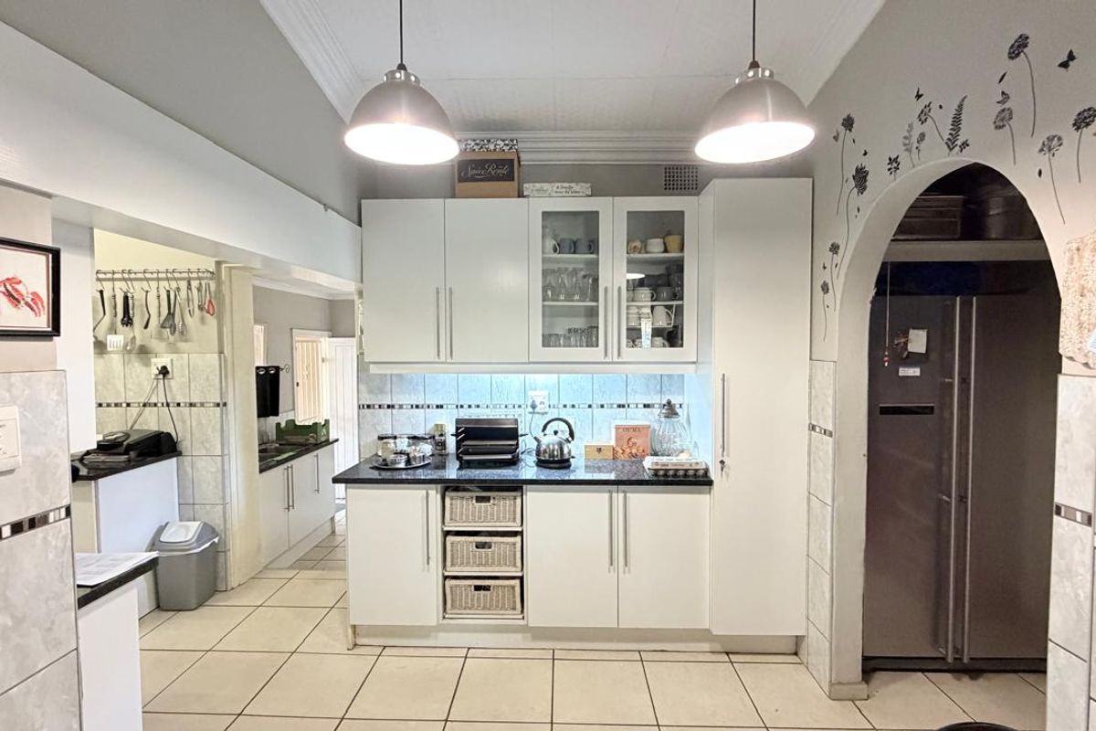 A functional kitchen featuring white cabinetry, granite countertops, tiled backsplash, and an arched entryway leading to a secondary prep area.