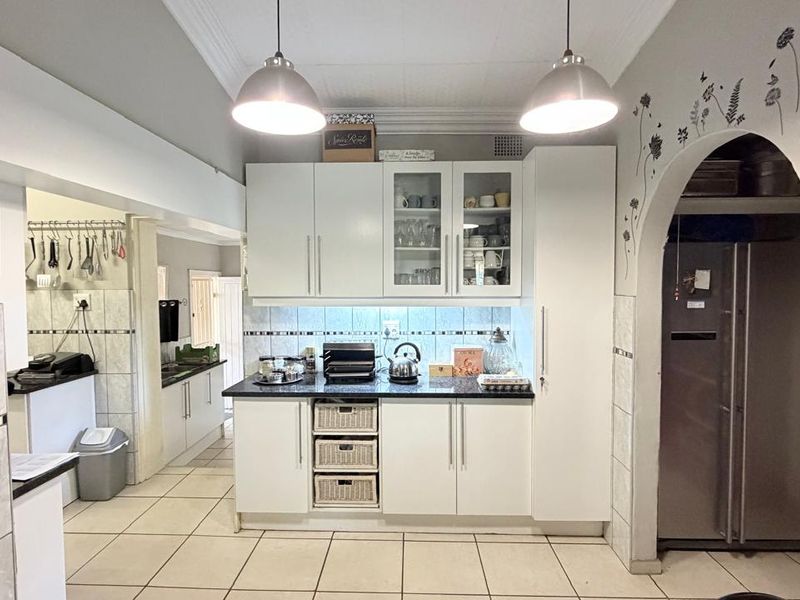 A functional kitchen featuring white cabinetry, granite countertops, tiled backsplash, and an arched entryway leading to a secondary prep area.