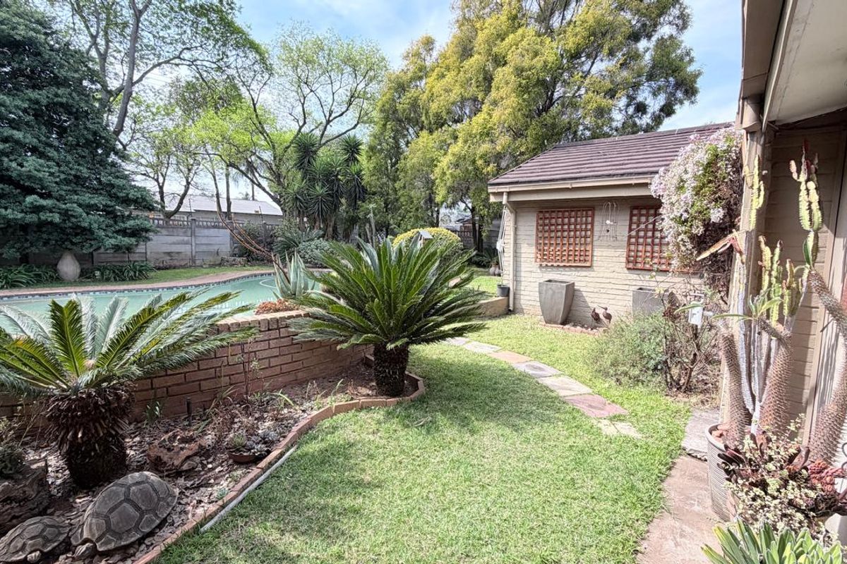 Rear garden area featuring a swimming pool, brick retaining wall, and established landscaping with a stone pathway leading alongside the house.
