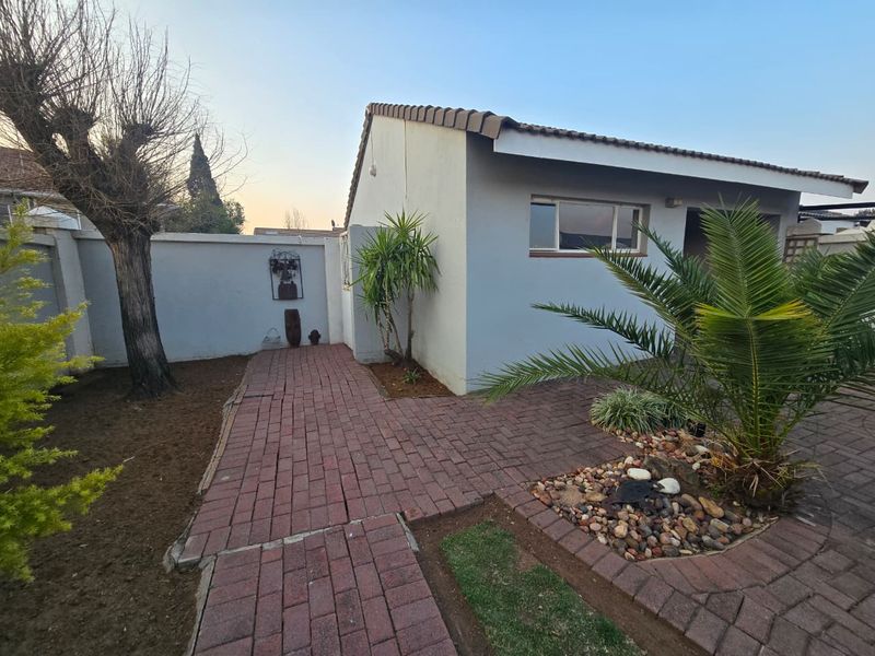 A rear exterior view of the townhouse featuring a paved walkway, perimeter wall, and established garden area with a tiled roof structure.