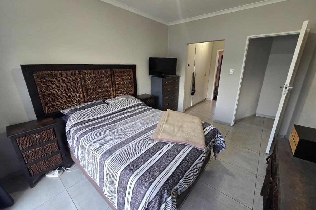 A functional bedroom featuring neutral tiled flooring, built-in storage cupboards, and simple cornice detailing, offering a clean and practical living space.