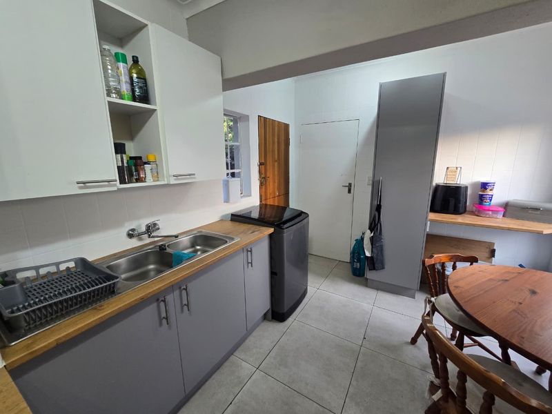 A functional kitchen featuring grey cabinetry, wooden countertops, a double basin sink, and tiled flooring, providing a practical workspace with ample storage.