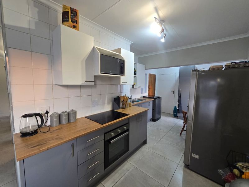 A functional kitchen featuring modern grey cabinetry, wood-look laminate countertops, a built-in oven with electric hob, and a tiled backsplash.