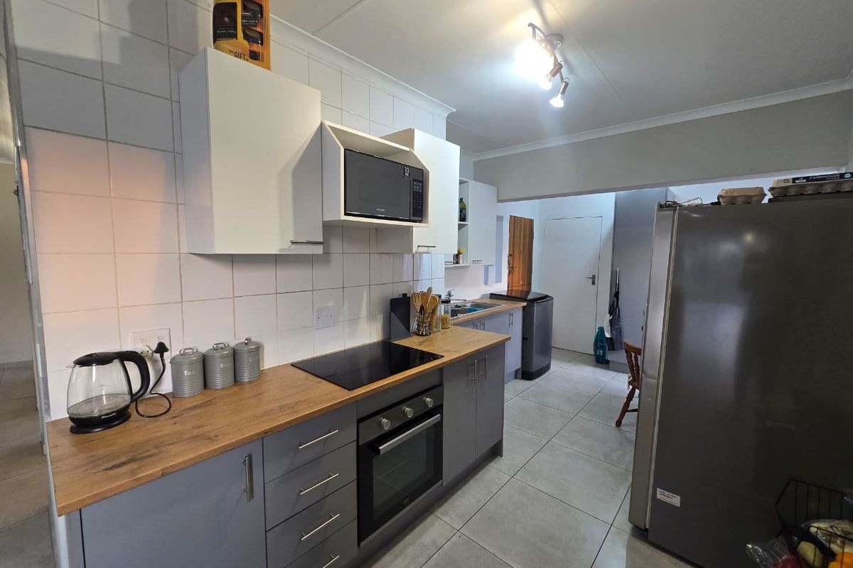 A functional kitchen featuring modern grey cabinetry, wood-look laminate countertops, a built-in oven with electric hob, and a tiled backsplash.