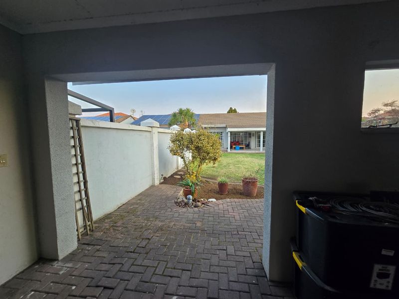 A covered patio area featuring brick paving and a view of the rear garden and boundary wall.