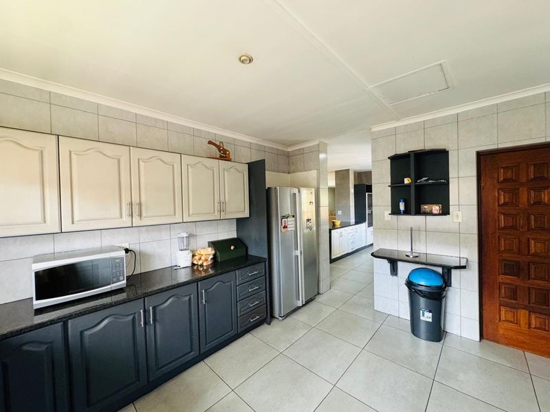 A functional kitchen featuring two-tone cabinetry, granite countertops, tiled backsplash, and tiled flooring, with a clear view into the adjacent living area.