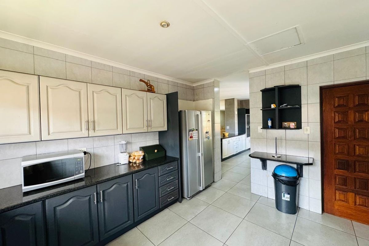A functional kitchen featuring two-tone cabinetry, granite countertops, tiled backsplash, and tiled flooring, with a clear view into the adjacent living area.