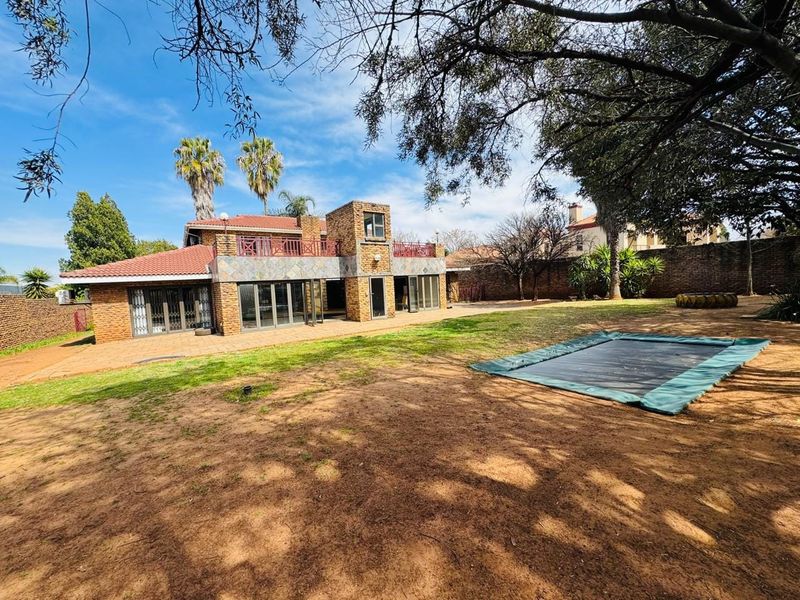 Rear view of a multi-level brick house featuring a tiled roof, upper balcony, and large sliding glass doors opening onto a paved patio and garden.