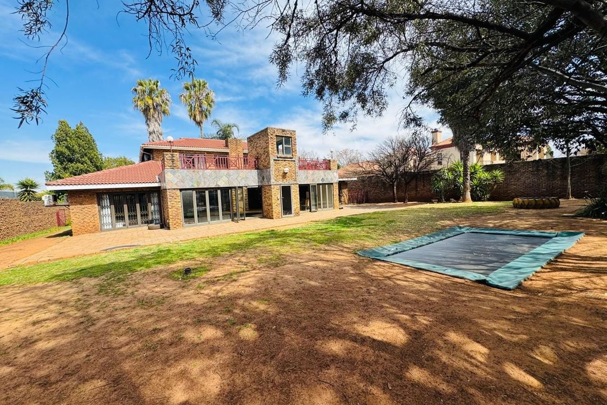 Rear view of a multi-level brick house featuring a tiled roof, upper balcony, and large sliding glass doors opening onto a paved patio and garden.