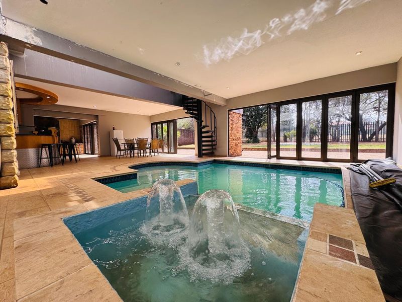 Spacious indoor pool area featuring built-in water fountains, a spiral staircase, and large bi-fold doors opening to the garden.