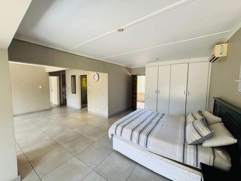 Spacious bedroom featuring large built-in cupboards, tiled flooring, and a wall-mounted air conditioning unit, with direct access to an adjoining area.