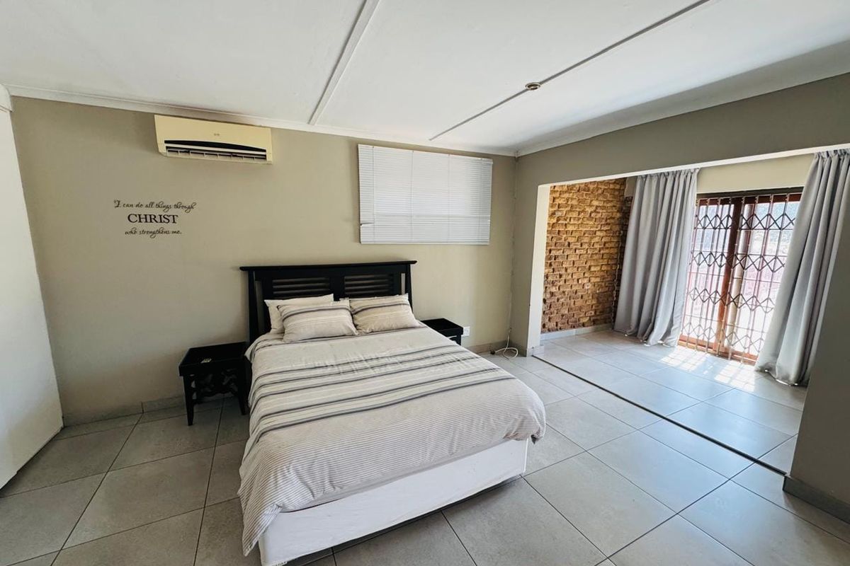 Spacious bedroom featuring tiled flooring, an exposed brick accent wall, split-system air conditioning, and direct access to an adjoining area through a security gate.