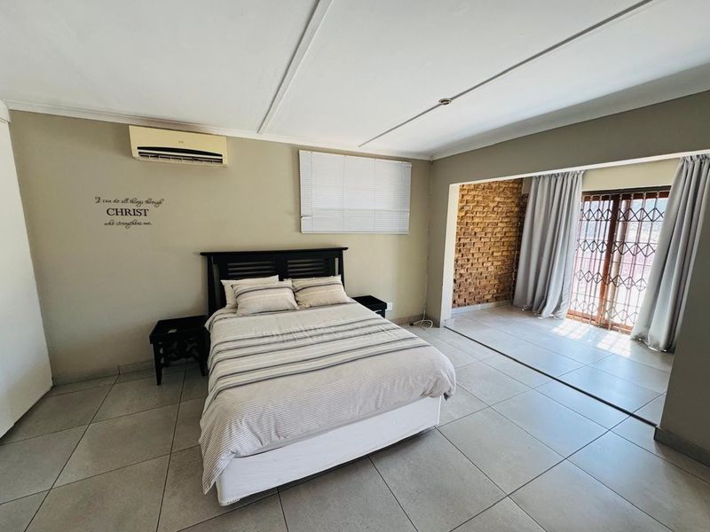 Spacious bedroom featuring tiled flooring, an exposed brick accent wall, split-system air conditioning, and direct access to an adjoining area through a security gate.