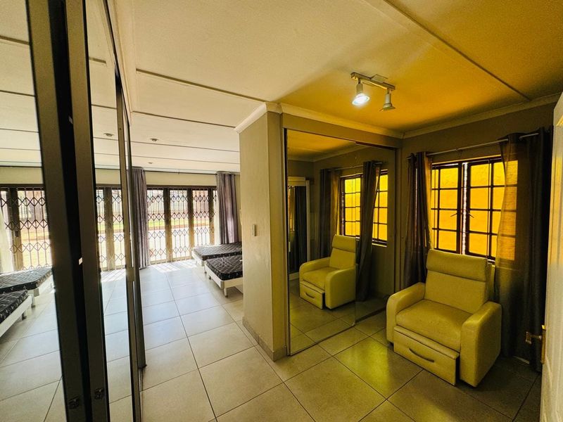 Spacious bedroom featuring tiled flooring, mirrored built-in cupboards, and security gates, offering a functional layout with ample natural light.