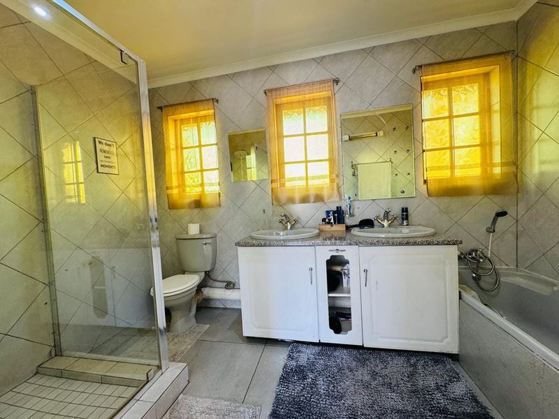 A dated bathroom featuring a double vanity, shower enclosure, bathtub, and toilet with tiled finishes throughout.