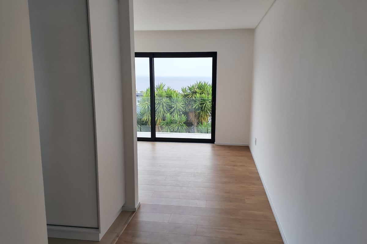 A bright, empty bedroom featuring modern laminate flooring, a built-in wardrobe, and large sliding glass doors opening to a balcony with scenic views.