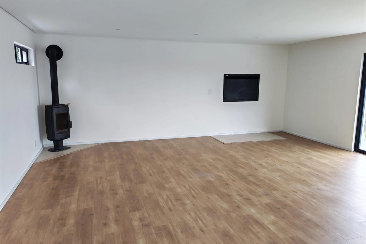 Spacious, empty living area featuring modern laminate wood flooring, a freestanding wood-burning stove, and a built-in wall fireplace.