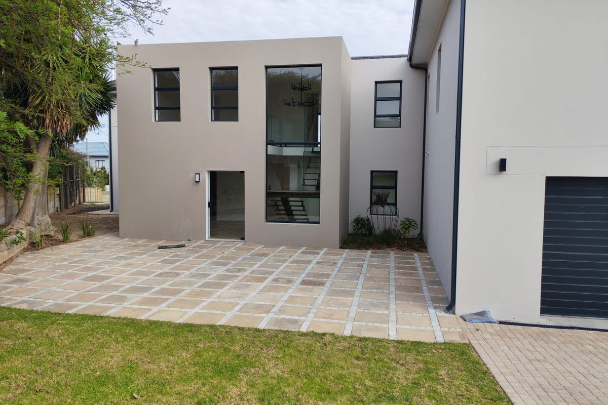Modern rear exterior view featuring a paved patio area, double-height glass window, and clean architectural lines.