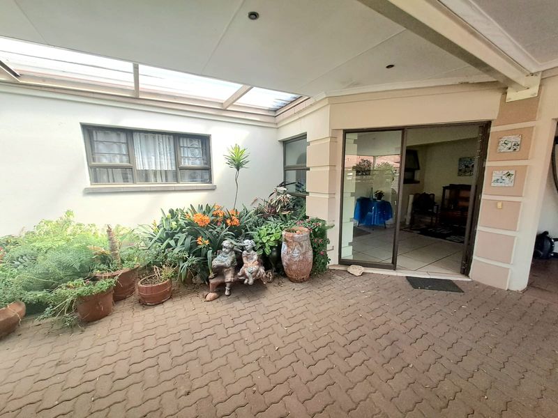 A covered patio area featuring paved flooring, a translucent roof structure, and sliding glass doors providing access to the interior living space.
