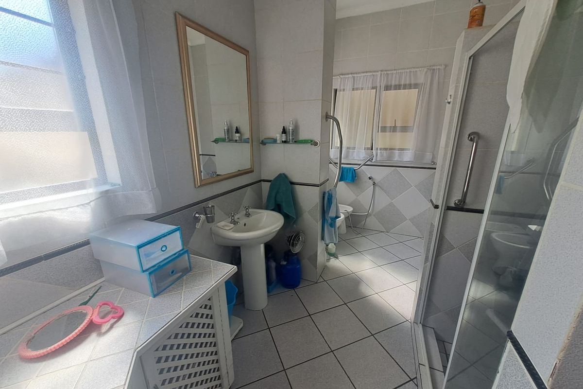 A functional bathroom featuring a pedestal basin, shower enclosure, and tiled finishes, equipped with safety grab rails.