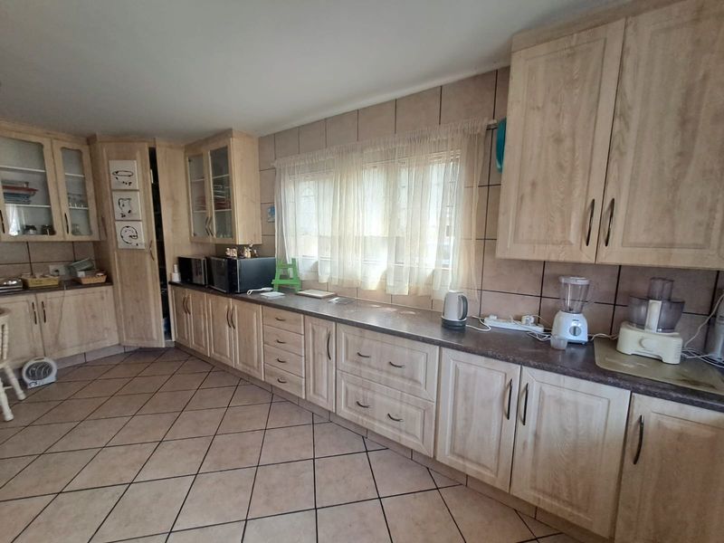 A functional kitchen featuring light wood-look laminate cabinetry, ample counter space, tiled backsplash, and durable floor tiles.