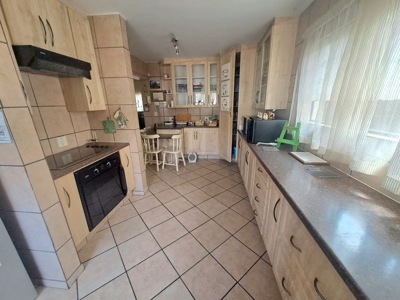 A functional kitchen featuring light wood-tone cabinetry, dark laminate countertops, ceramic tile flooring, and integrated appliances including an oven and hob.