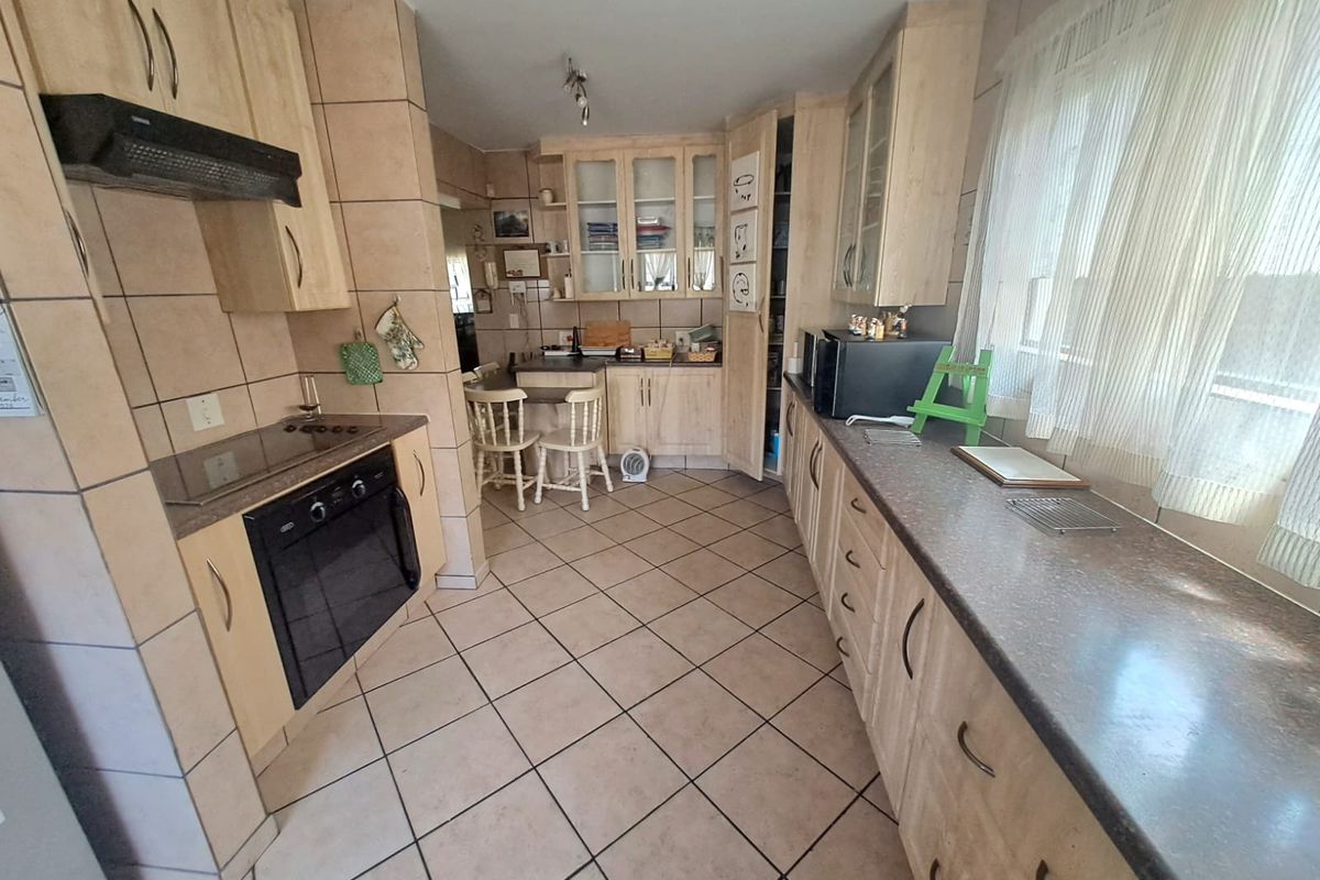 A functional kitchen featuring light wood-tone cabinetry, dark laminate countertops, ceramic tile flooring, and integrated appliances including an oven and hob.