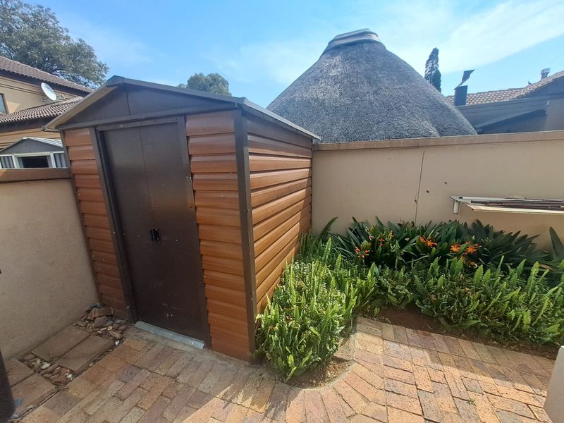 Rear garden area featuring a metal storage shed, brick paving, and established garden beds against a boundary wall.