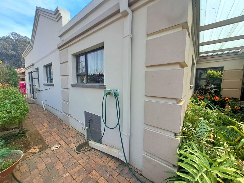 Rear exterior view of the townhouse featuring brick paving, a covered patio area, and established garden beds along the building facade.