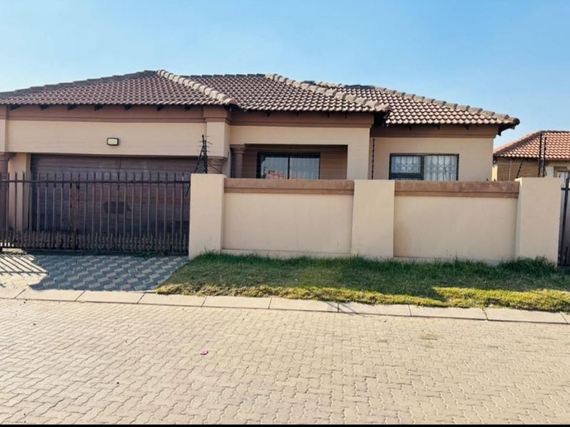 Front elevation of a single-story house featuring a tiled roof, paved driveway, secure perimeter wall with electric fencing, and a private garage.