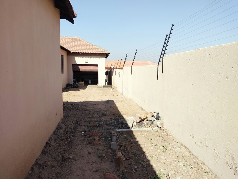 Side yard area featuring a perimeter wall with electric fencing, leading towards a garage entrance with a roll-up door.