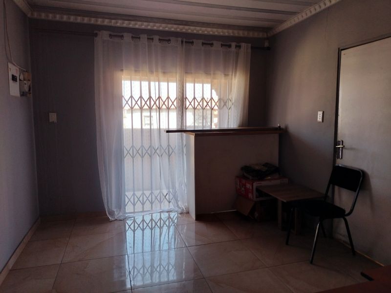 A living area featuring tiled flooring, crown molding, and a built-in counter, with a security gate leading to the exterior.