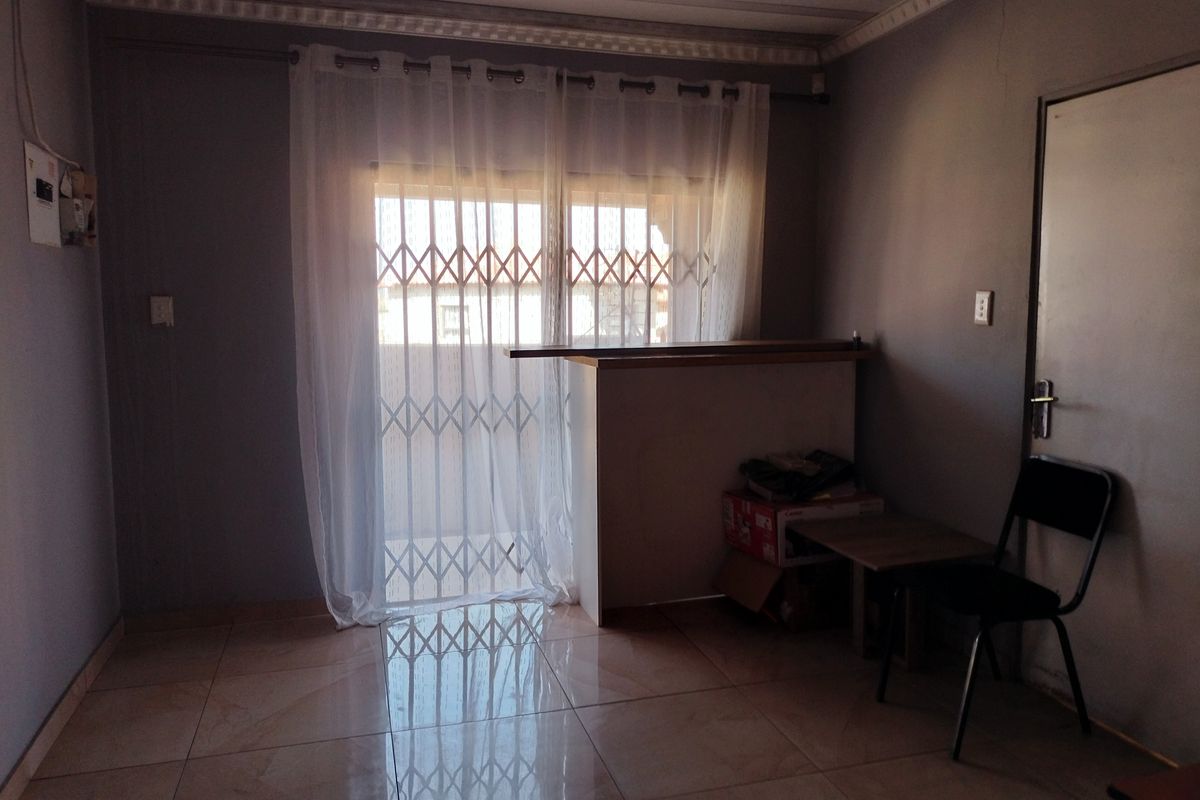 A living area featuring tiled flooring, crown molding, and a built-in counter, with a security gate leading to the exterior.