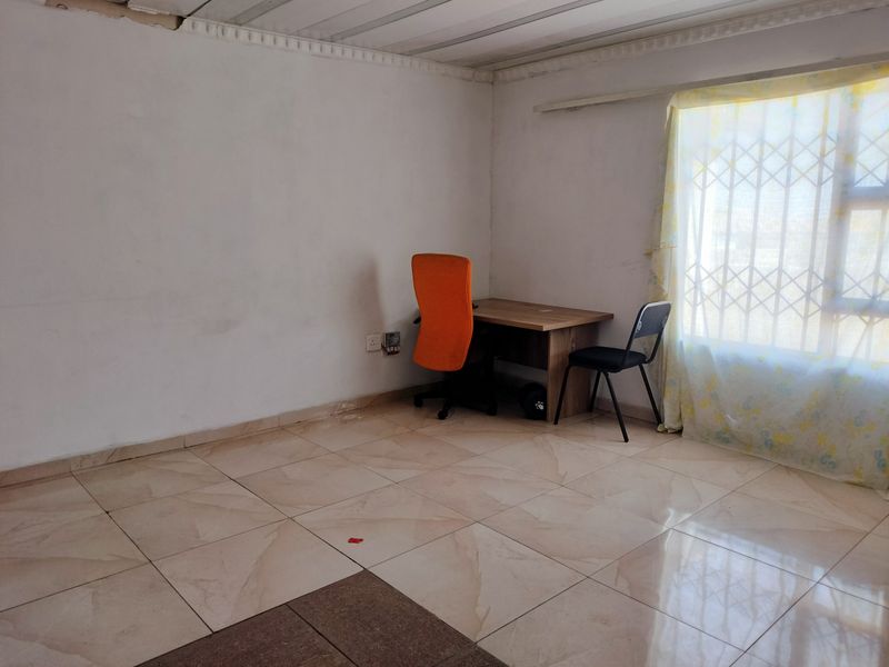 A bedroom featuring tiled flooring, security gate on the window, and basic wall finishes, currently used as a small home office space.