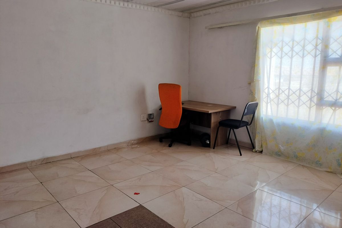 A bedroom featuring tiled flooring, security gate on the window, and basic wall finishes, currently used as a small home office space.