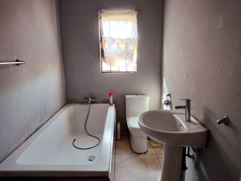 A functional bathroom featuring a bathtub, pedestal basin, and toilet, with tiled flooring and a window providing natural light.
