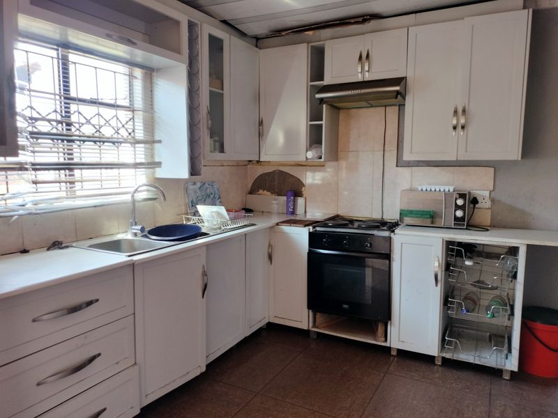 A functional kitchen featuring white cabinetry, built-in oven and hob, and tiled flooring. The space requires some maintenance and cosmetic updates to improve its condition.