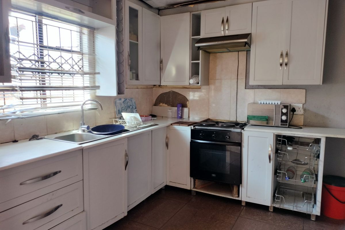 A functional kitchen featuring white cabinetry, built-in oven and hob, and tiled flooring. The space requires some maintenance and cosmetic updates to improve its condition.