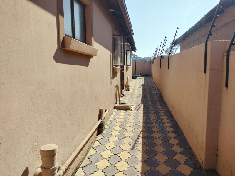 A narrow side passage featuring paved flooring, perimeter walling with electric fencing, and exposed exterior plumbing infrastructure.