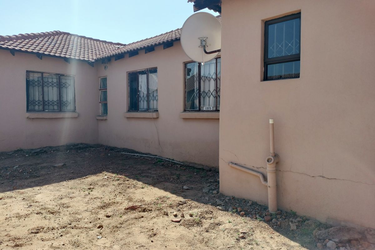 Rear exterior view of the house showing tiled roofing, security bars on windows, and visible cracks in the exterior wall plaster.