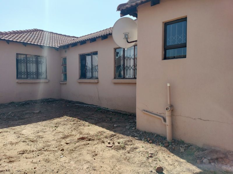 Rear exterior view of the house showing tiled roofing, security bars on windows, and visible cracks in the exterior wall plaster.