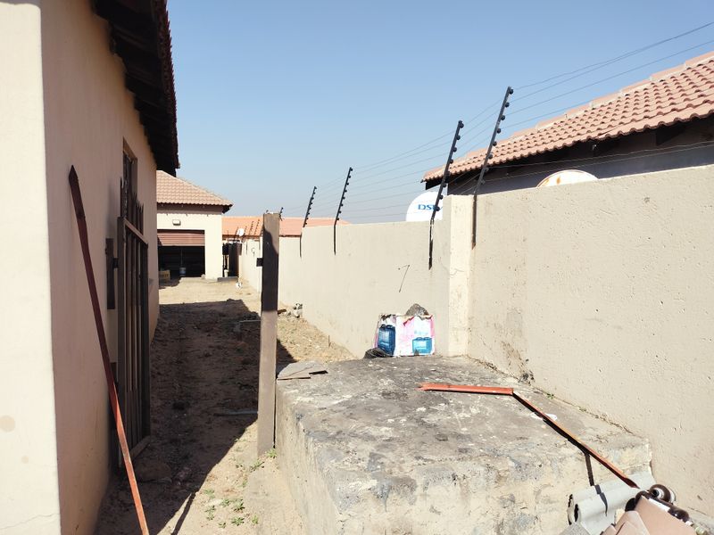 A view of the side and rear exterior area featuring a perimeter wall with electric fencing and a concrete plinth structure.