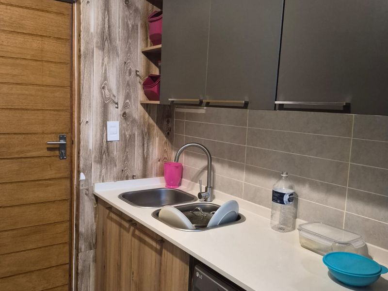 A functional laundry area featuring modern grey and wood-tone cabinetry, a stainless steel sink, stone countertops, and tiled backsplash.