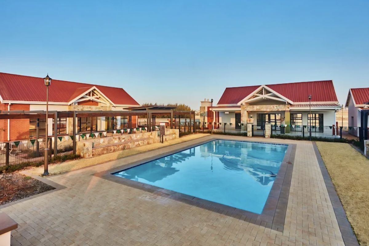 A well-maintained communal pool area featuring a paved deck, stone-clad architectural details, and covered pergola structures within a townhouse complex.