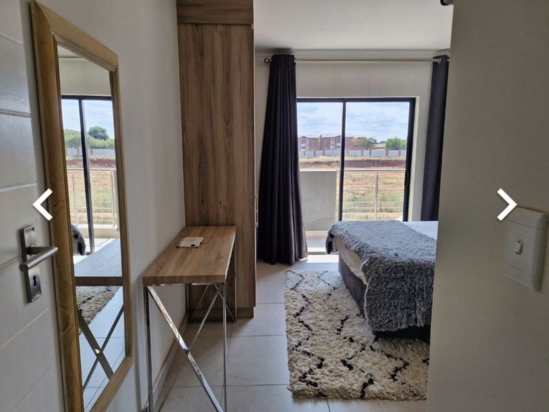 A well-lit bedroom featuring built-in cabinetry, tiled flooring, and a sliding glass door leading to a private balcony with exterior views.