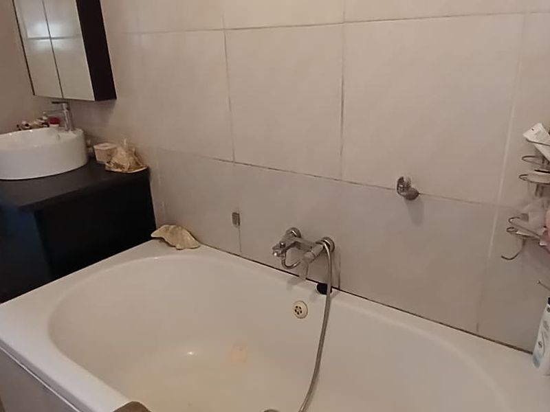 A functional bathroom featuring a built-in vanity with a vessel sink, a bathtub with a handheld shower attachment, and tiled wall finishes.