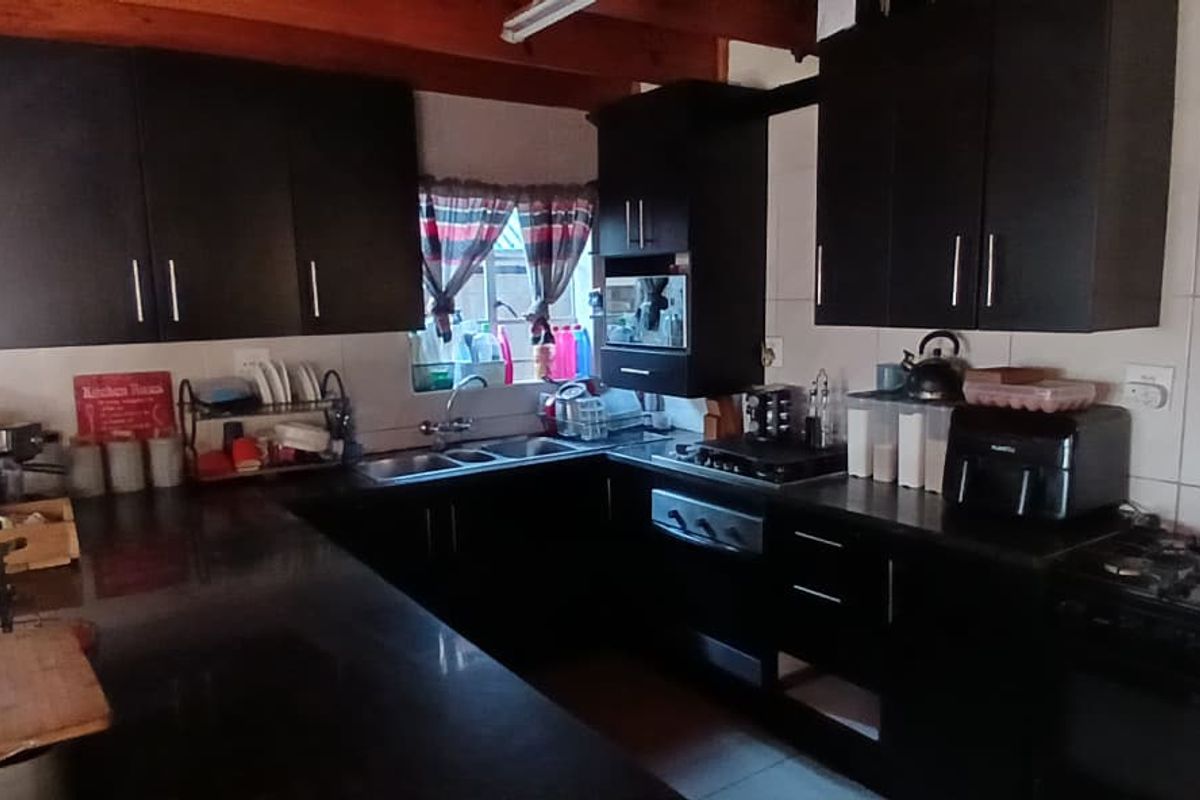 A functional kitchen featuring dark cabinetry, a double sink, gas hob, electric oven, and exposed timber ceiling beams with tiled splashbacks.