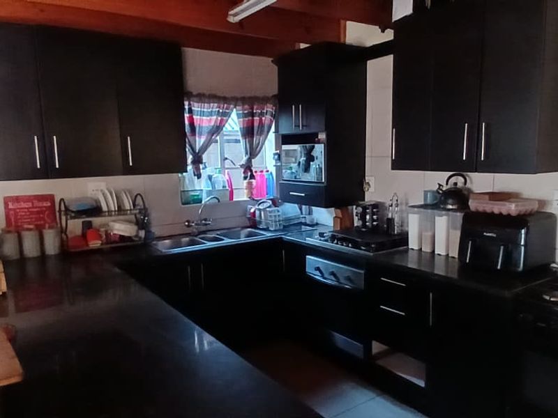 A functional kitchen featuring dark cabinetry, a double sink, gas hob, electric oven, and exposed timber ceiling beams with tiled splashbacks.