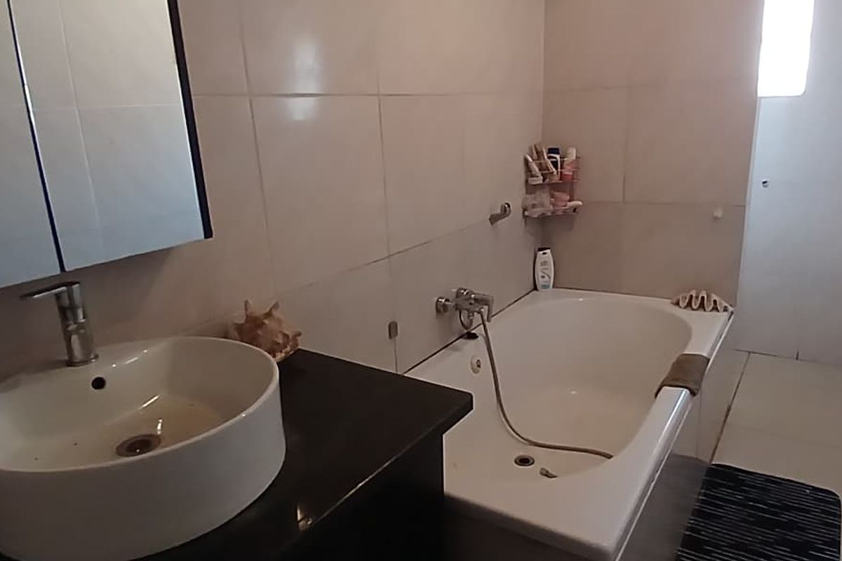 A functional bathroom featuring a vessel sink on a dark vanity, a bathtub with shower mixer, and neutral wall tiling.