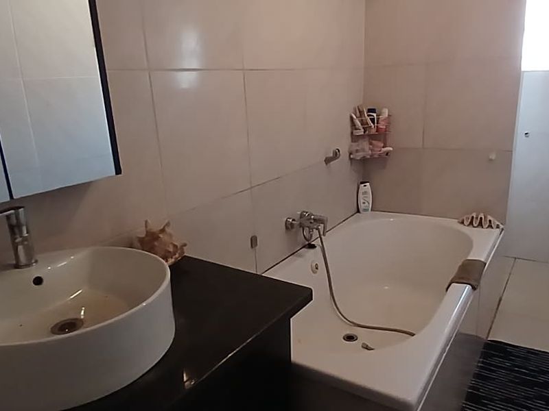 A functional bathroom featuring a vessel sink on a dark vanity, a bathtub with shower mixer, and neutral wall tiling.